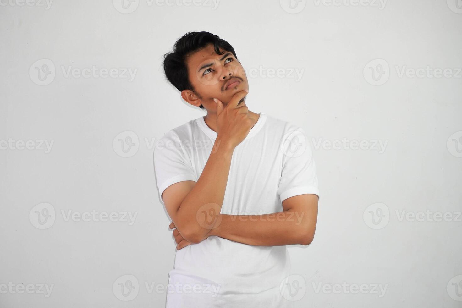 thinking young asian man holding chin thinking gesture, looking for idea wearing white t shirt isolated on white background photo