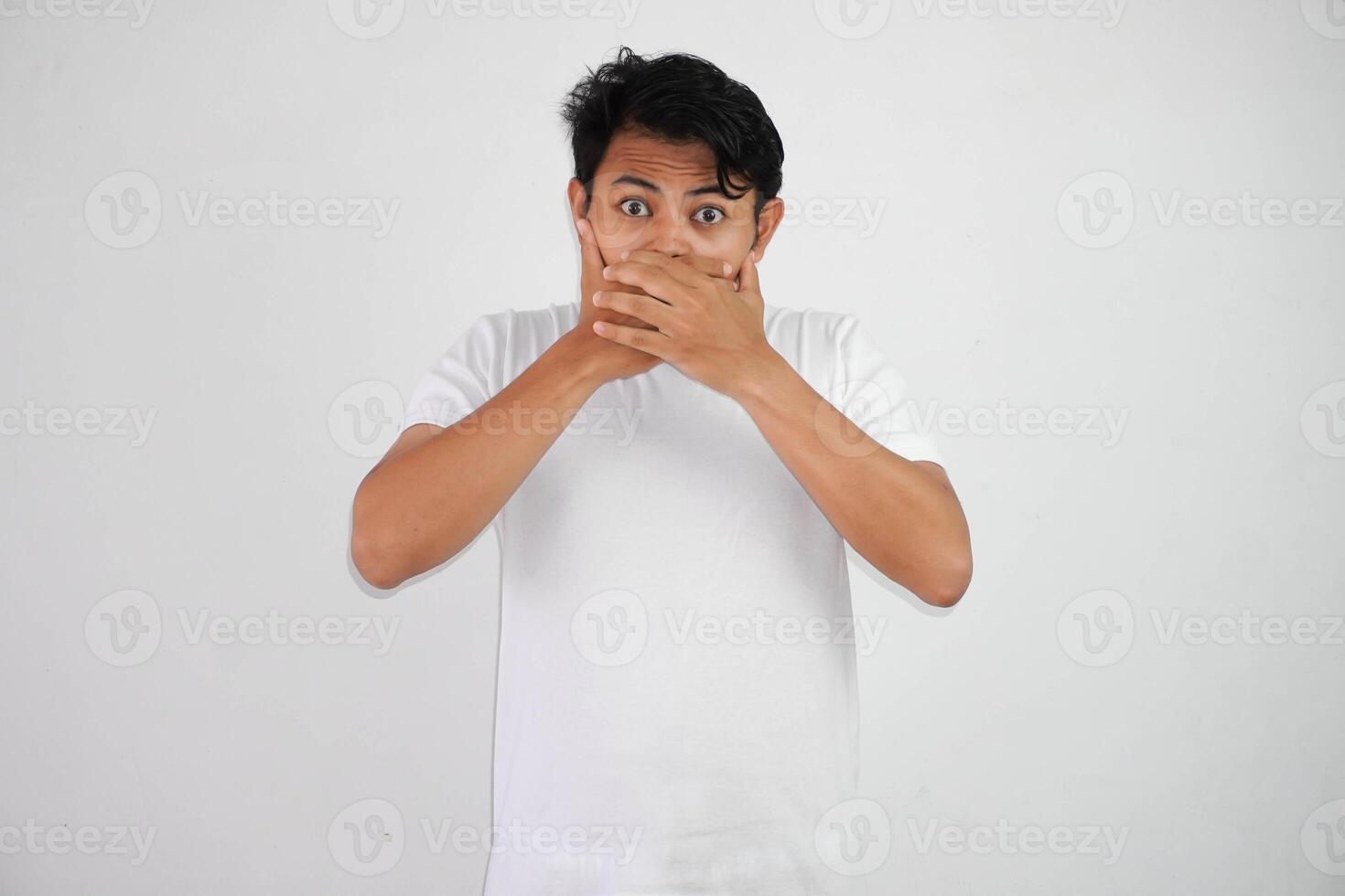 Portrait of scared young Asian man covering mouth with hands wearing white t shirt isolated on white background photo