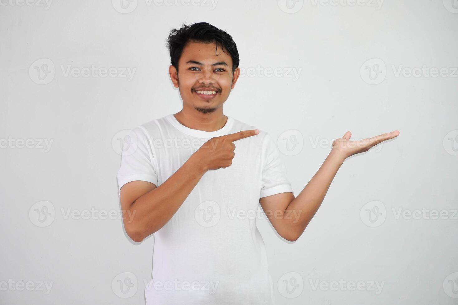 smiling asian man with an open hand with fingers pointing to the side wearing white t shirt isolated on white background photo