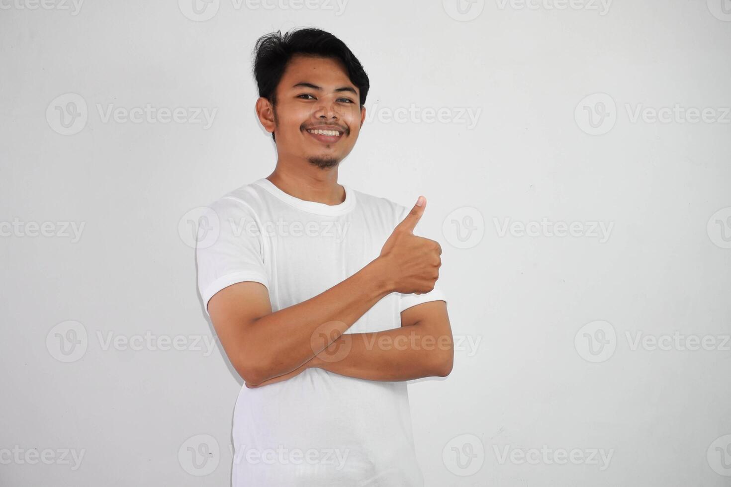 retrato de alegre asiático hombre en vistiendo blanco t camisa sonriente y demostración pulgares arriba a cámara aislado terminado blanco antecedentes foto