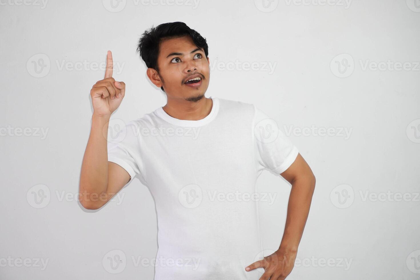 Excited young Asian man pointing fingers up having a good idea with copy space wearing white t shirt isolated on white background photo