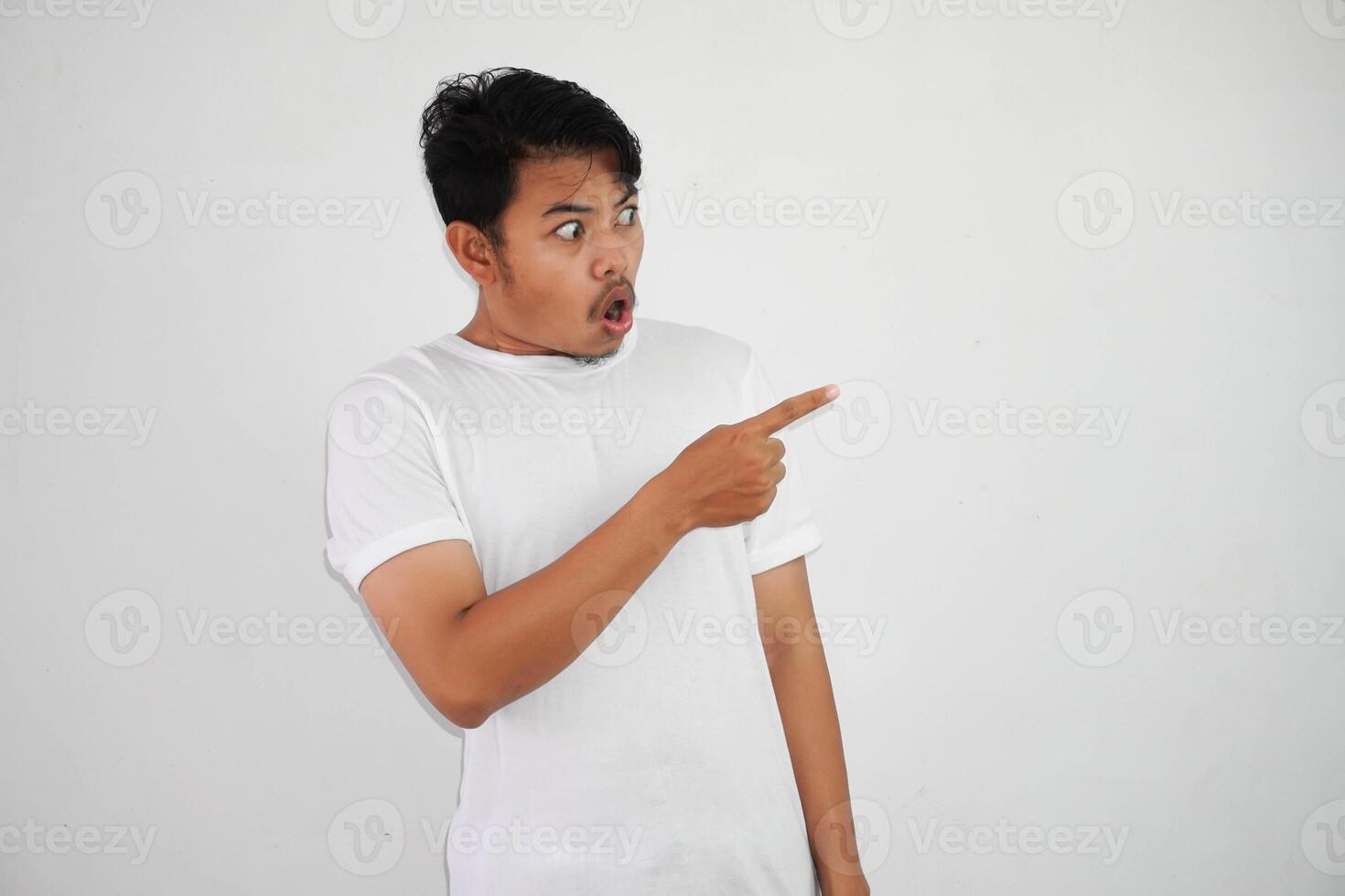 shocked asian man with fingers pointing to the side wearing white t shirt isolated on white background photo