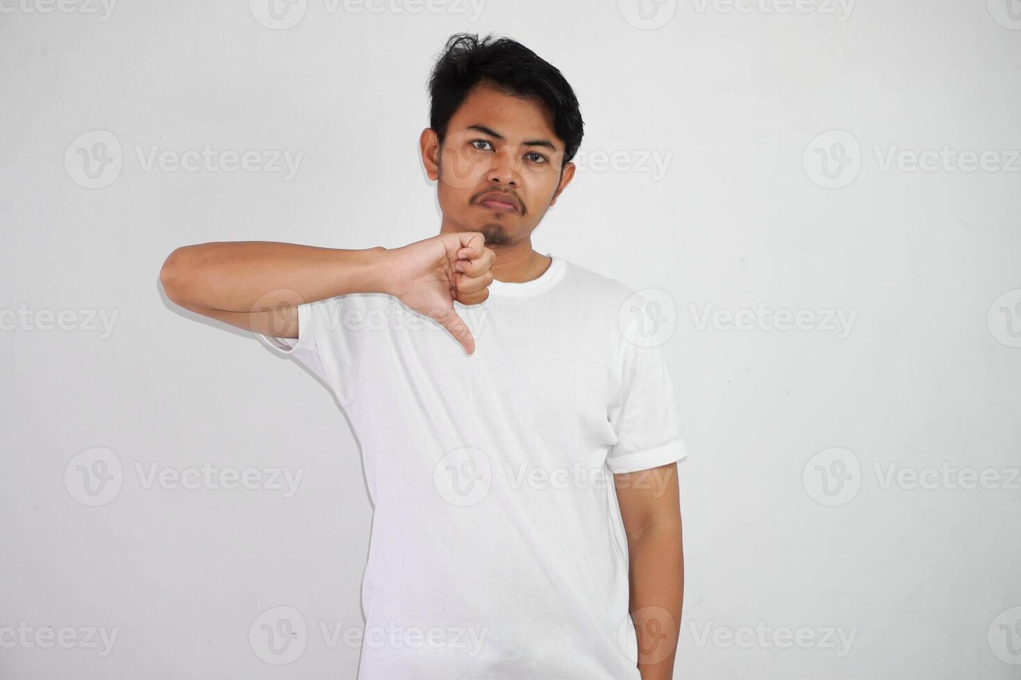 Angry young Asian man showing rejection and negative with thumbs down gesture wearing white t shirt isolated on white background photo