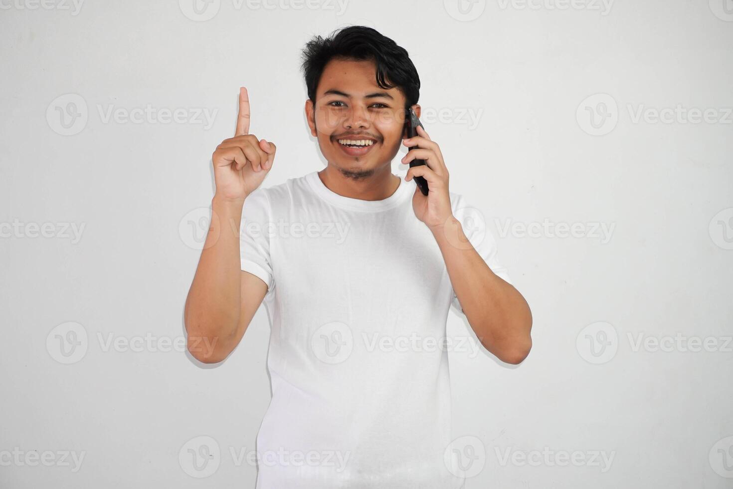 Excited young Asian man pointing fingers up having a good idea with while calling wearing white t shirt isolated on white background photo