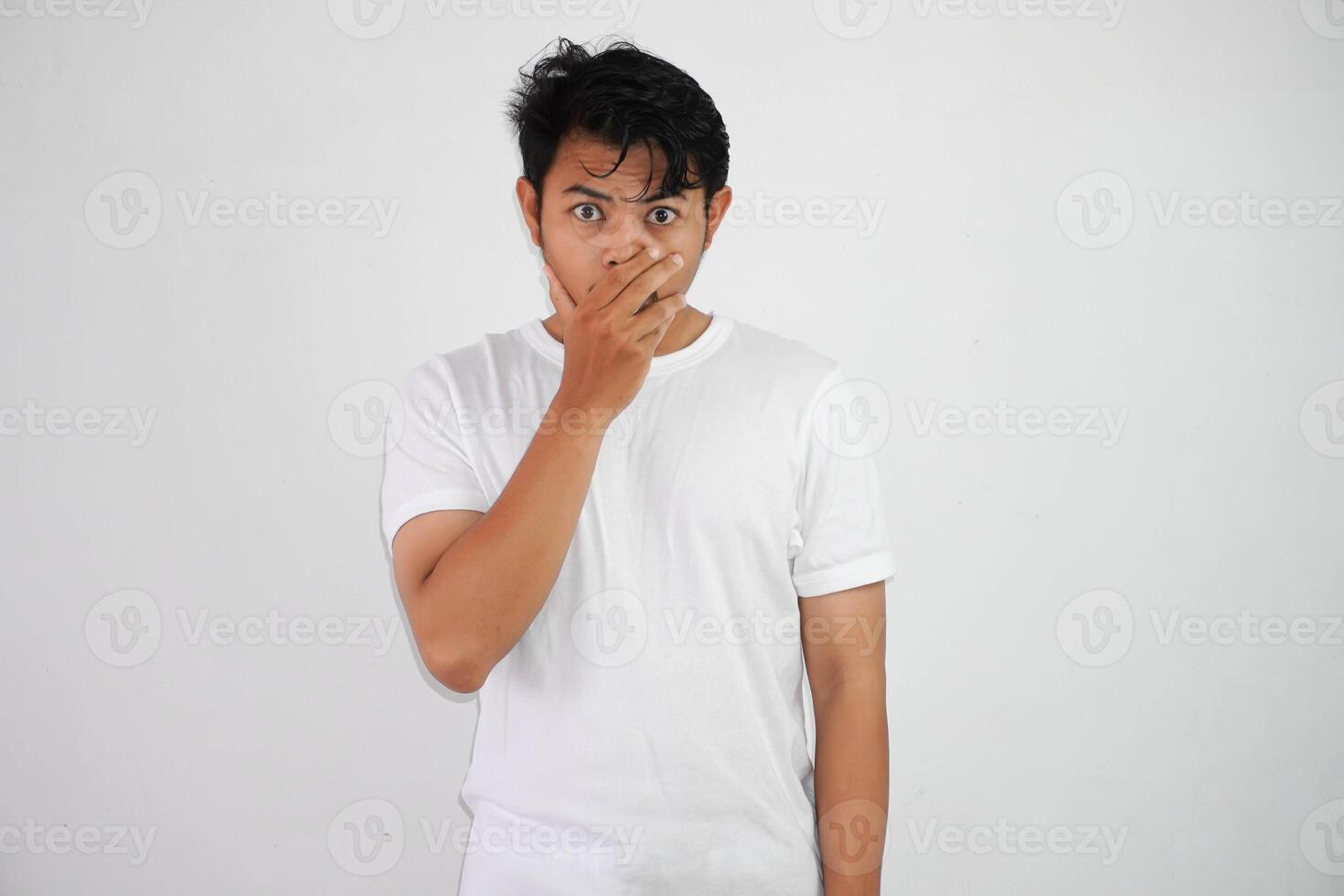 Portrait of scared young Asian man covering mouth with hands wearing white t shirt isolated on white background photo