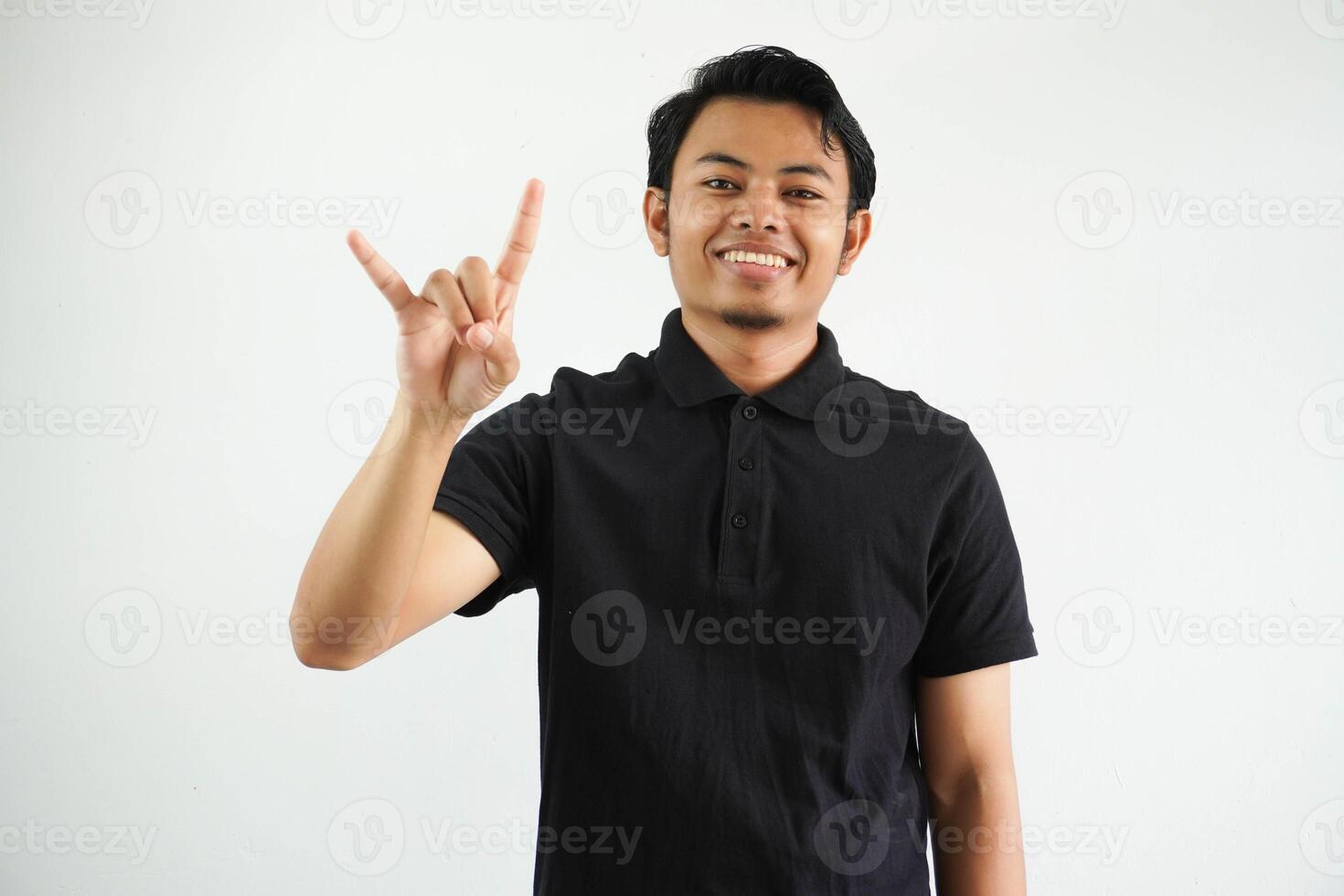 smiling Young handsome asian man wearing black polo t shirt and shouting with crazy expression doing gesture rock symbol with hands up. Music star. Heavy concept. isolated on white background photo