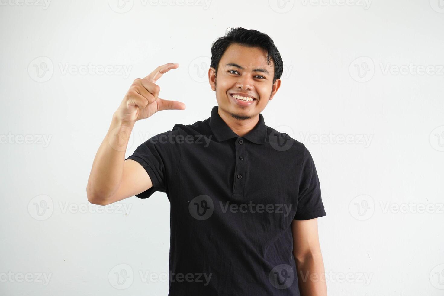 young asian man posing on a white backdrop holding something little with forefingers, smiling and confident, wearing black polo t shirt. photo