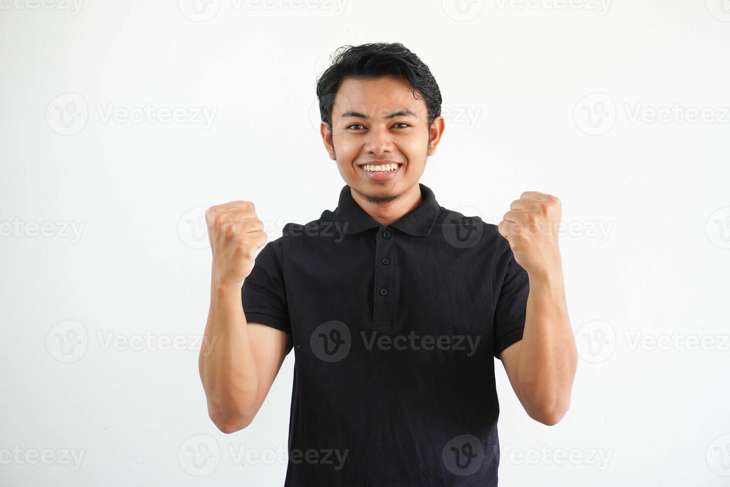 smiling or happy young asian man clenched his fists cheering carefree and excited. Victory concept, wearing black polo t shirt isolated on white background photo