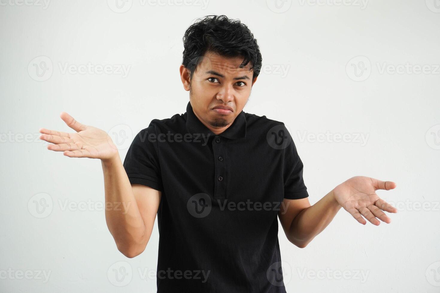 Portrait of handsome young asian man confused puzzled man shrugging shoulders wearing black polo t shirt isolated over white background photo