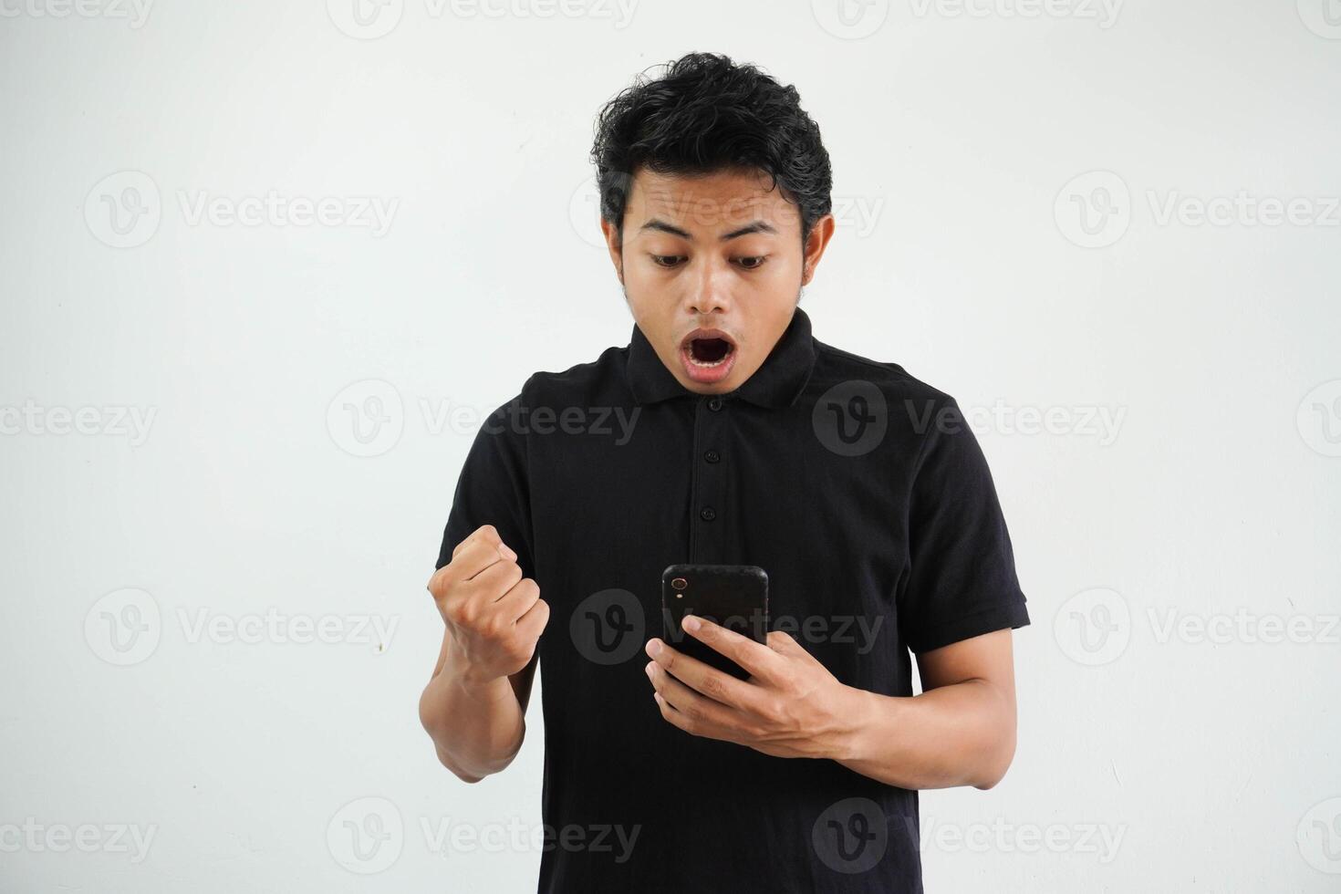 surprised or shocked young asian man isolated on white background holding phone and hands in fists with sending a message photo