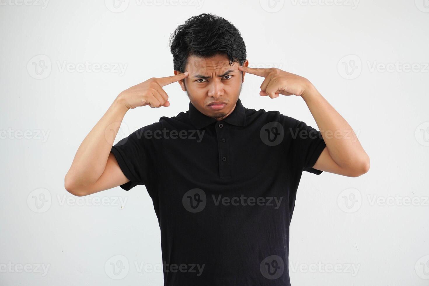 young asian man posing on a white backdrop focused on a task, keeping forefingers pointing head. photo