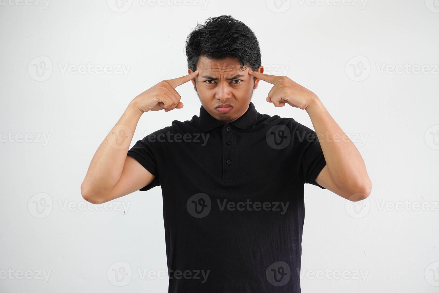 young asian man posing on a white backdrop focused on a task, keeping forefingers pointing head. photo