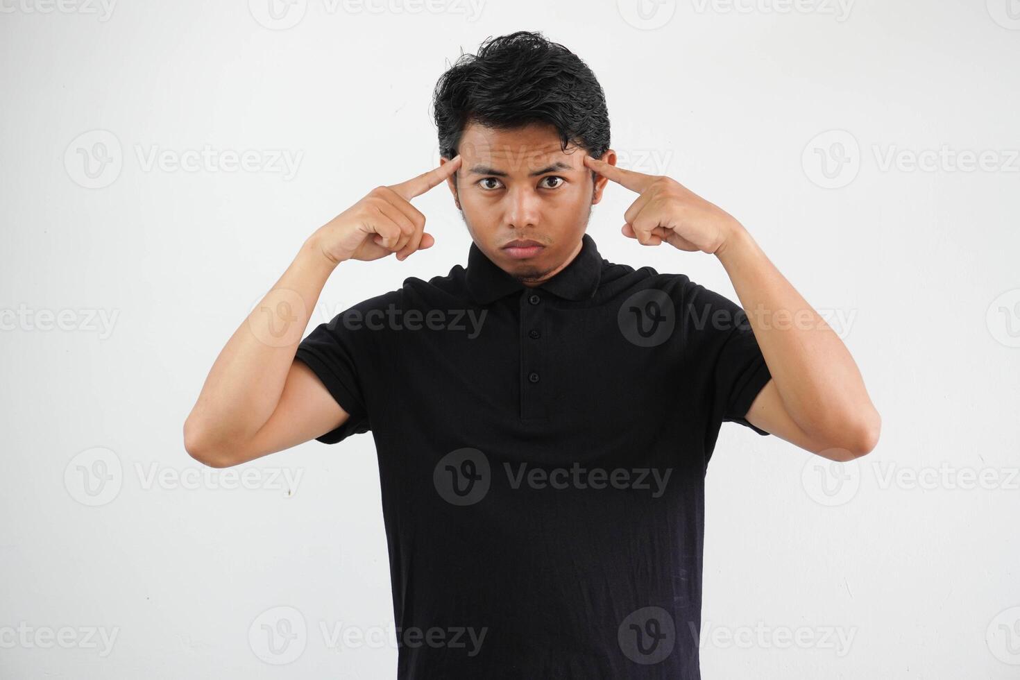 young asian man posing on a white backdrop focused on a task, keeping forefingers pointing head. photo