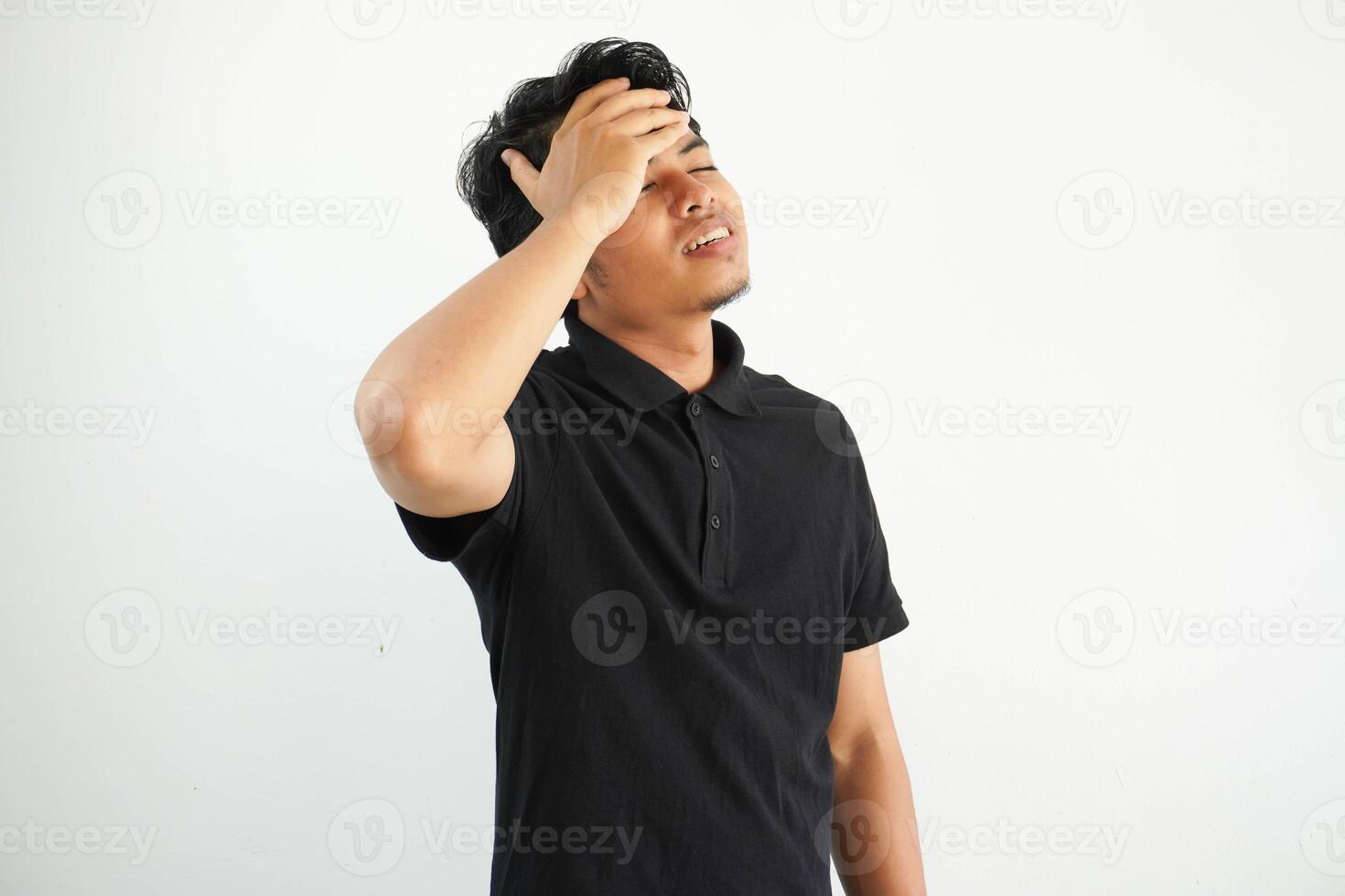 sorprendido joven asiático hombre con negro pelo sonriente y participación su manos en el cabeza, sensación emocionado vistiendo negro polo t camisa aislado en blanco antecedentes foto