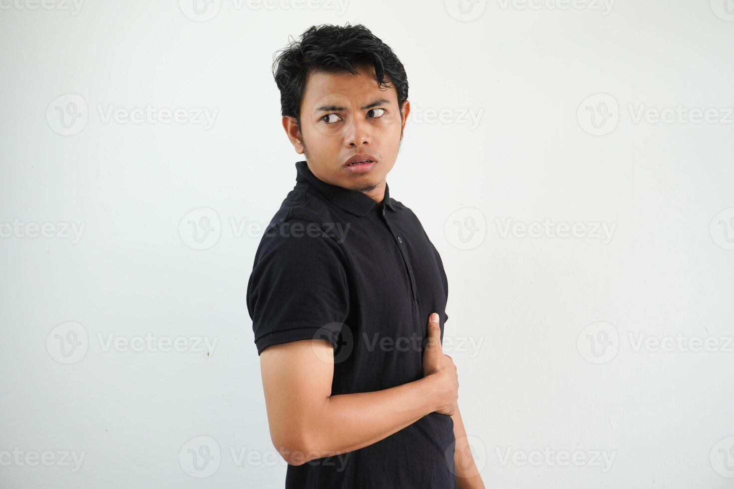 young asian man posing on a white backdrop looks aside smiling, cheerful and pleasant. wearing black polo t shirt. photo