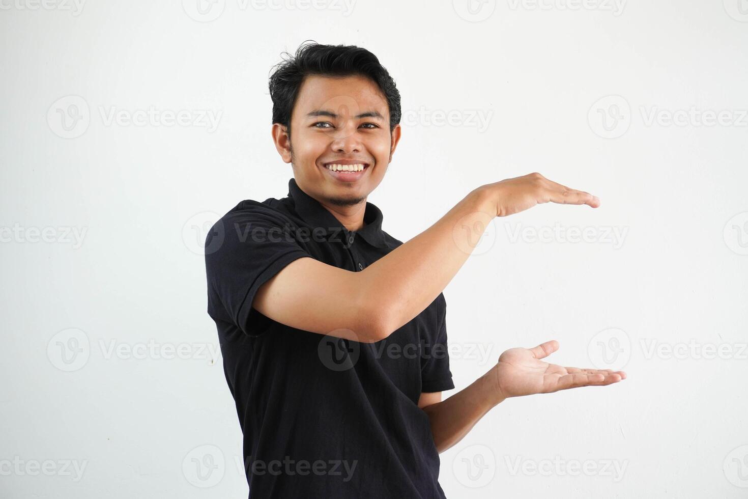 joven asiático hombre posando en un blanco fondo sonriente y felicidad participación un Copiar espacio Entre manos, vistiendo negro polo t camisa. foto