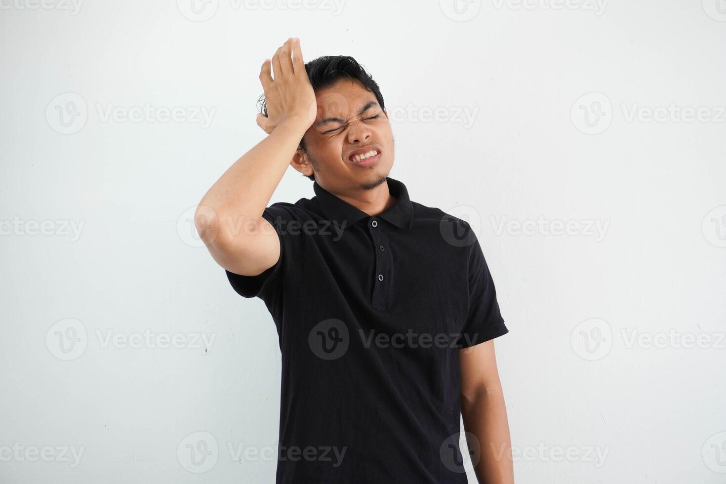 Portrait of young asian man isolated on white background suffering from severe headache, pressing fingers to temples, closing eyes to relieve pain with helpless face expression photo