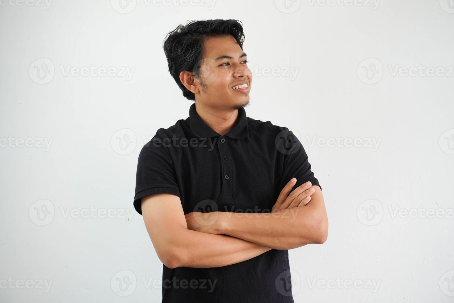 joven asiático hombre sonriente contento a el cámara con brazos cruzado vistiendo negro polo t camisa aislado en blanco antecedentes foto
