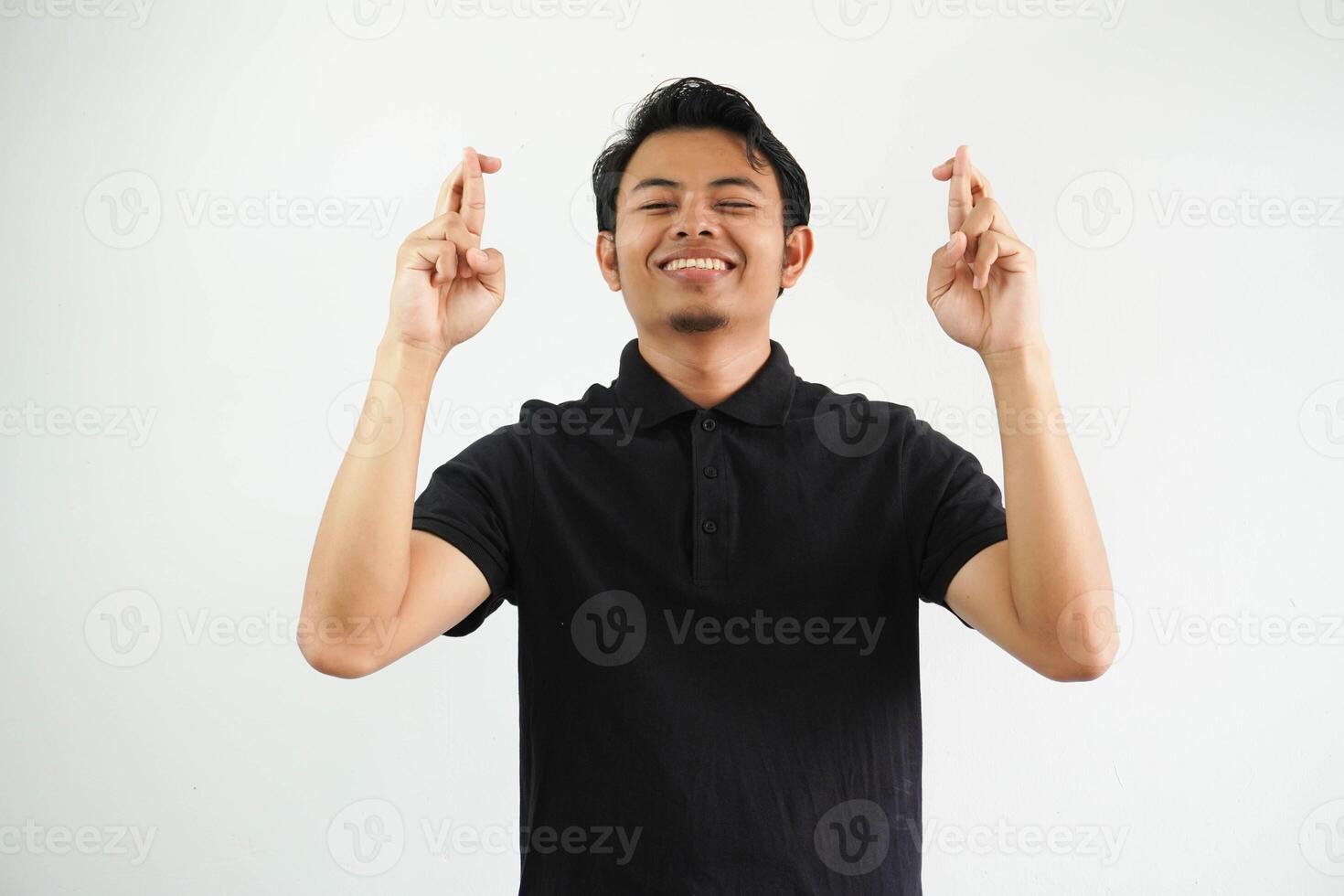 sonriente joven hermoso asiático hombre aislado cruce dedos para teniendo suerte vistiendo negro polo t camisa. foto