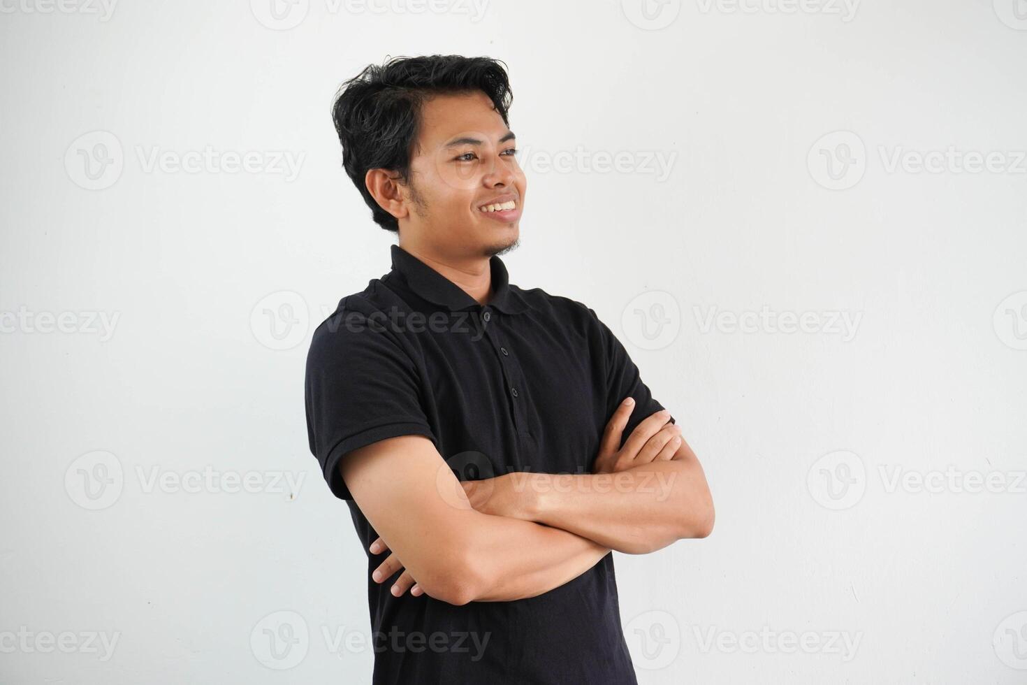 joven asiático hombre sonriente contento a el cámara con brazos cruzado vistiendo negro polo t camisa aislado en blanco antecedentes foto