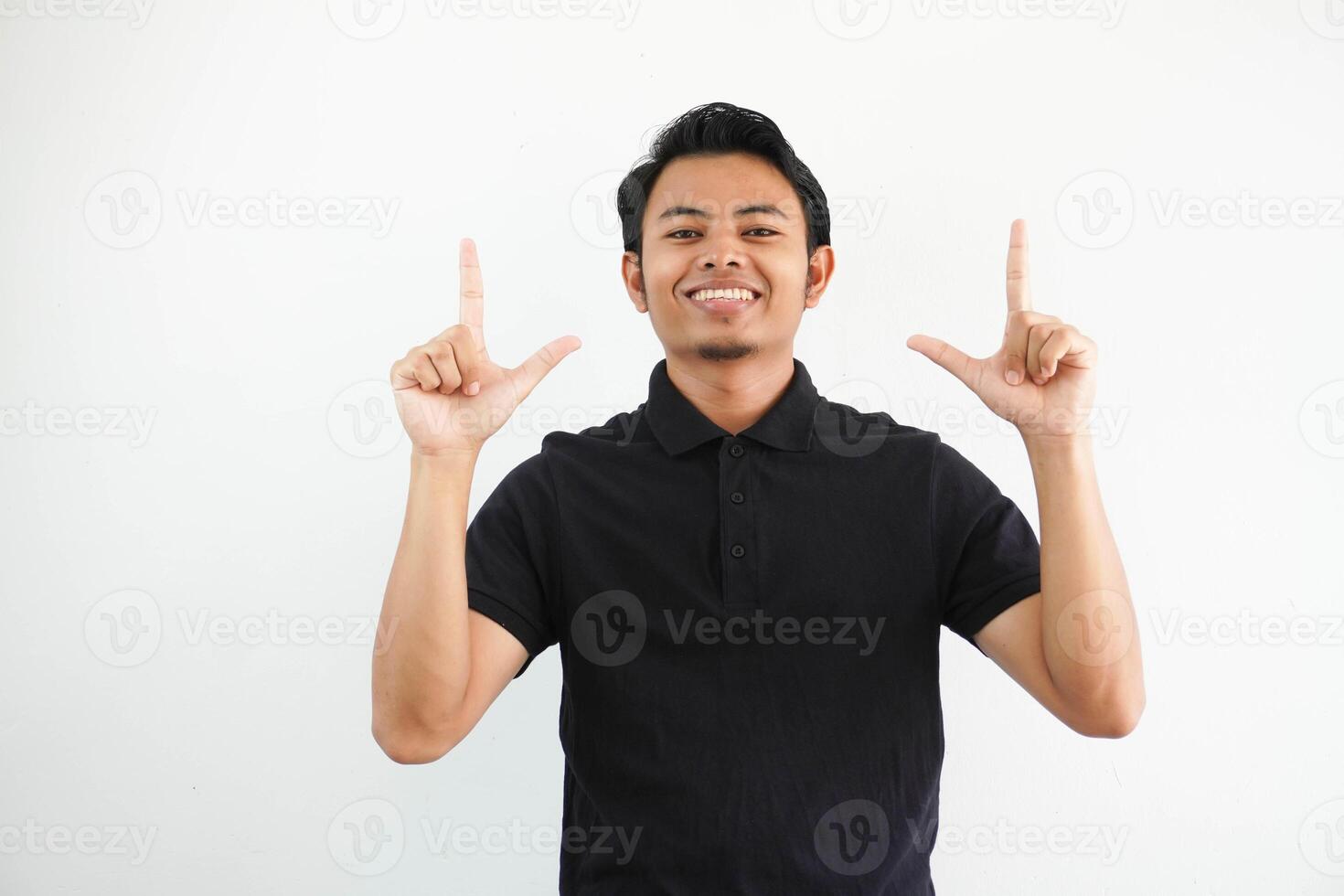 young Asian man smiling happy and pointing both hands up wearing black polo t shirt isolated on white background photo