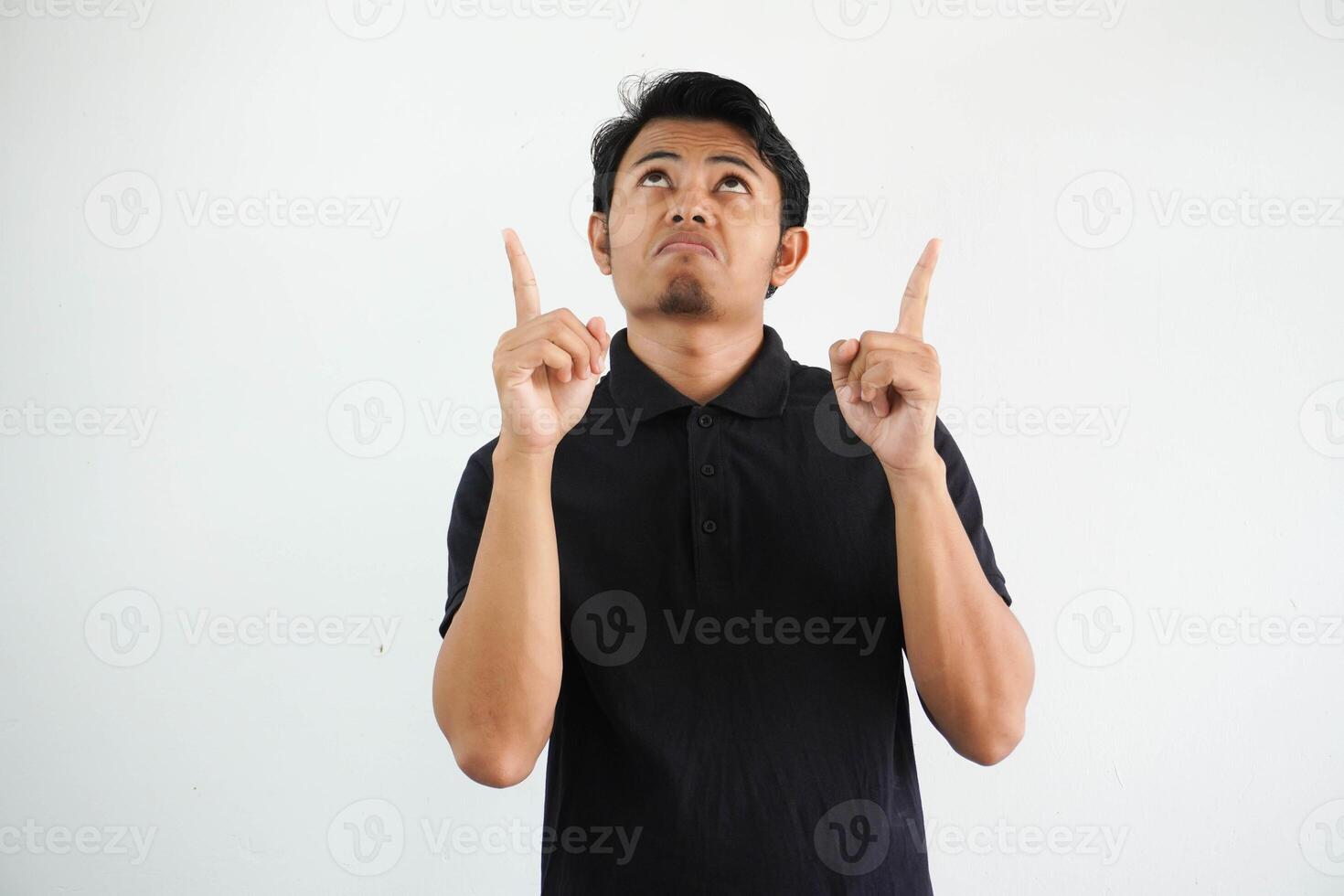 joven asiático hombre confuso y señalando ambos manos arriba vistiendo negro polo t camisa aislado en blanco antecedentes foto