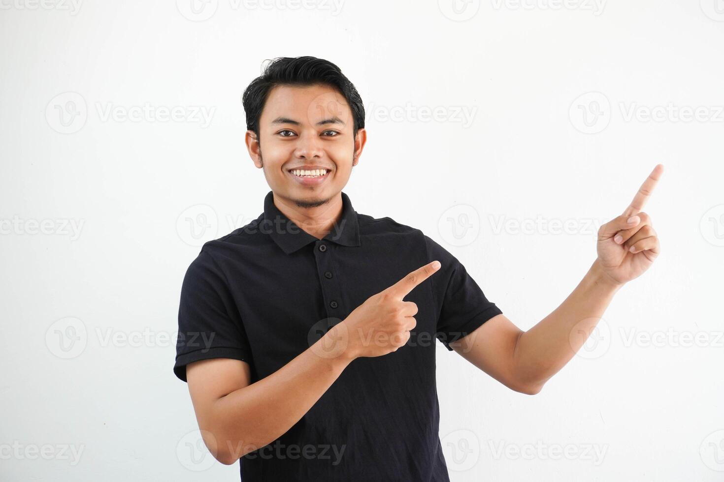 young asian man smiling confident with both hand pointing to the left side wearing black polo t shirt isolated white background photo