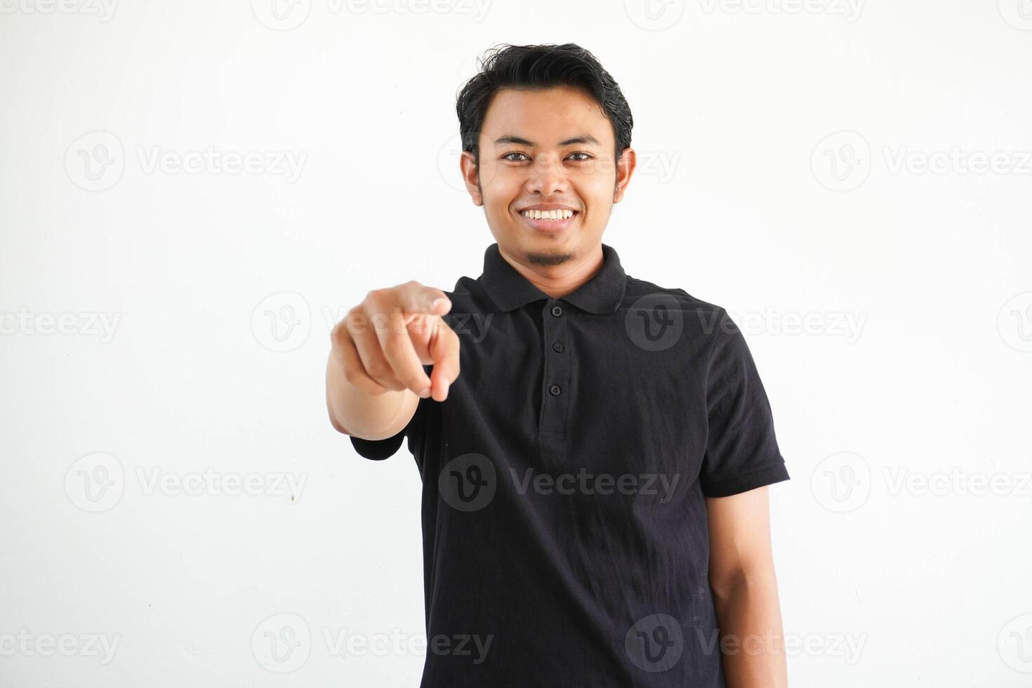 young Asian man smiling and pointing towards camera wearing black polo t shirt isolated on white background. photo