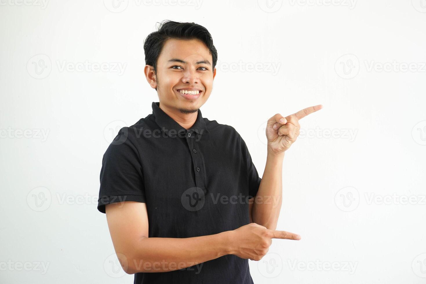 young asian man smiling confident with both hand pointing to the left side wearing black polo t shirt isolated white background photo