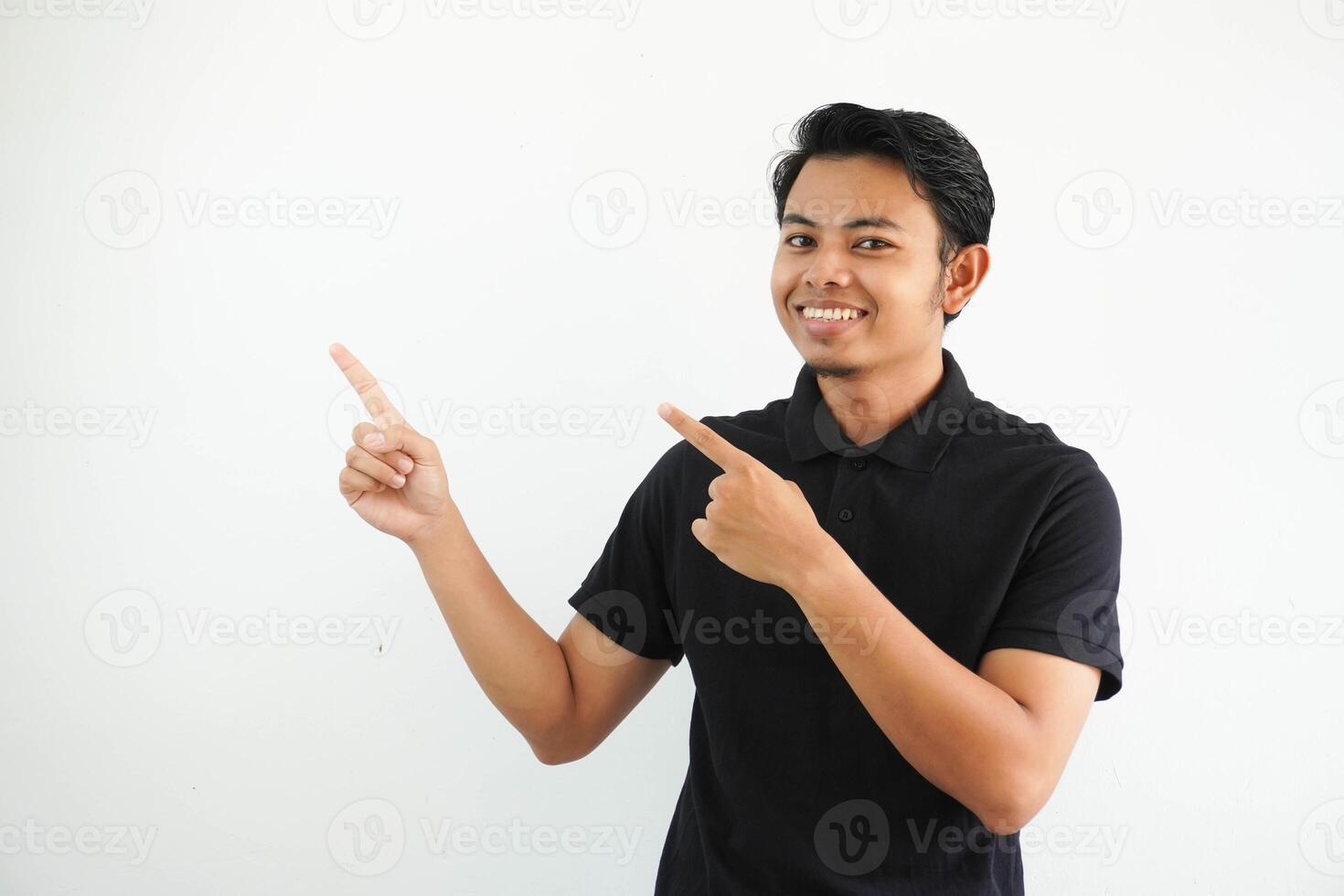 young asian man smiling confident with both hand pointing to the right side wearing black polo t shirt isolated white background photo