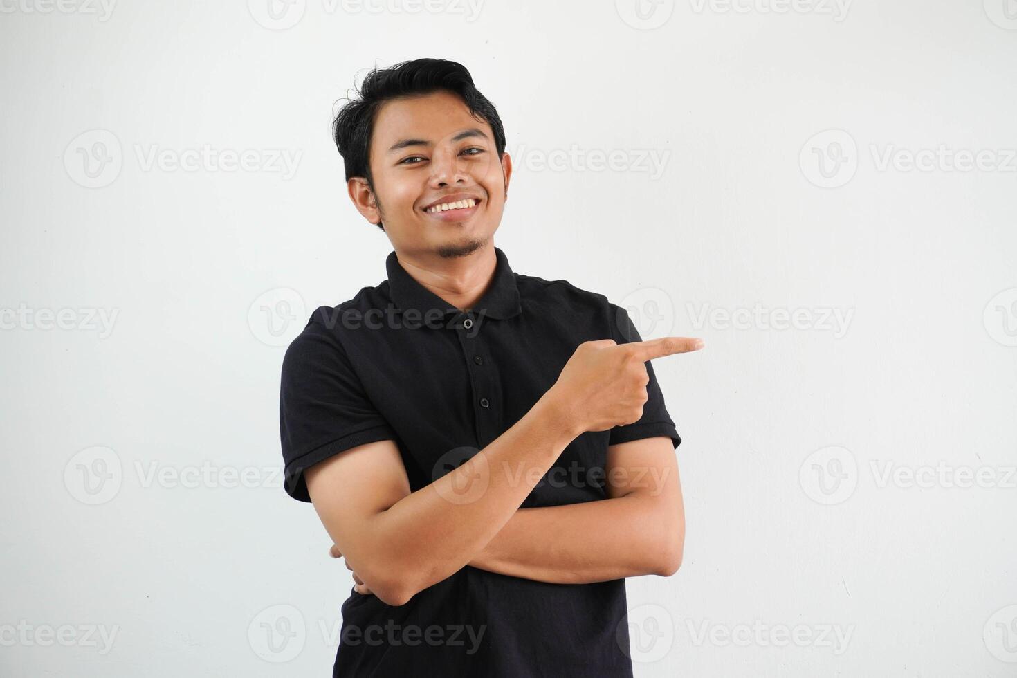 young asian man smiling confident with hand pointing to the left side wearing black polo t shirt isolated white background photo