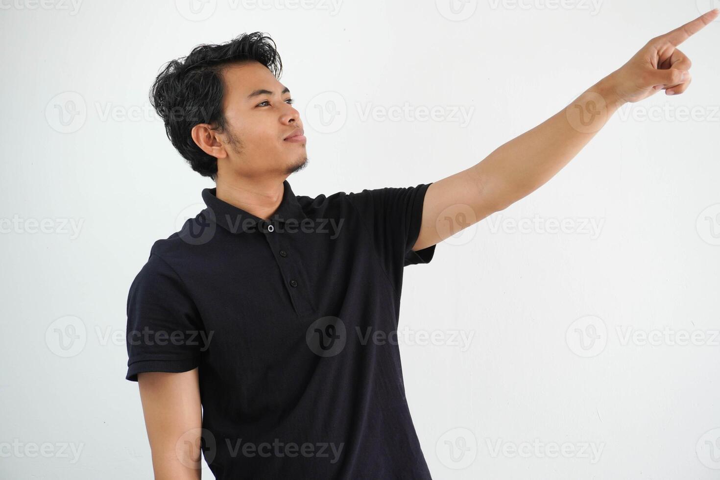 young asian man smiling confident with hand pointing to the left side wearing black polo t shirt isolated white background photo