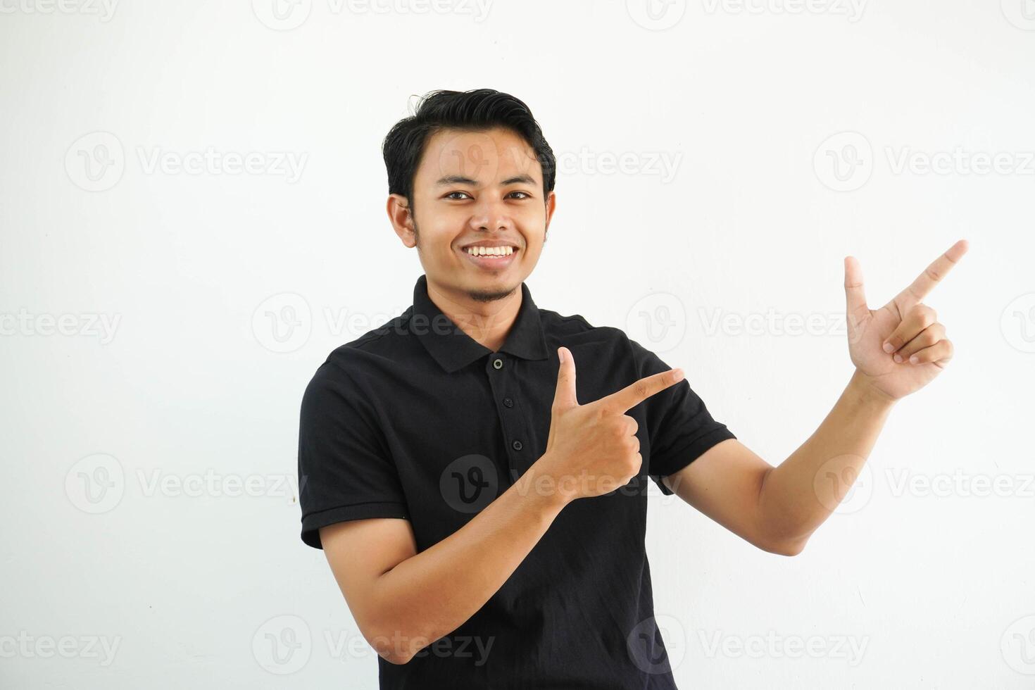young asian man smiling confident with both hand pointing to the left side wearing black polo t shirt isolated white background photo