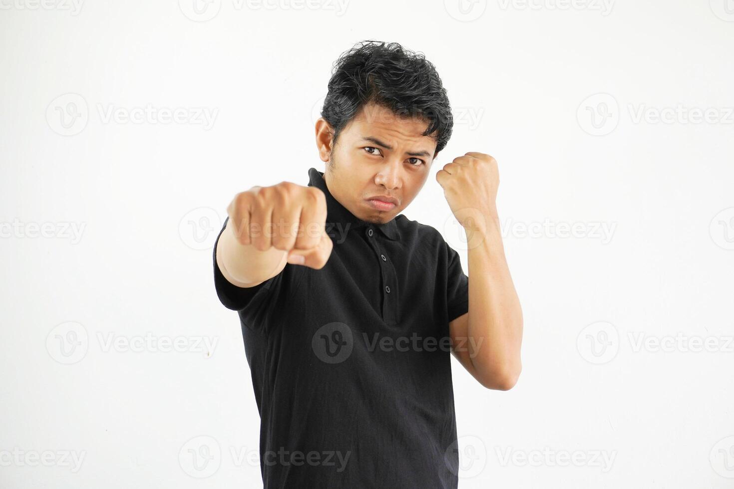 joven asiático hombre en contra un blanco estudio fondo, lanzamiento un puñetazo, enojo, luchando debido a un argumento, boxeo, vistiendo negro polo t camisa. foto