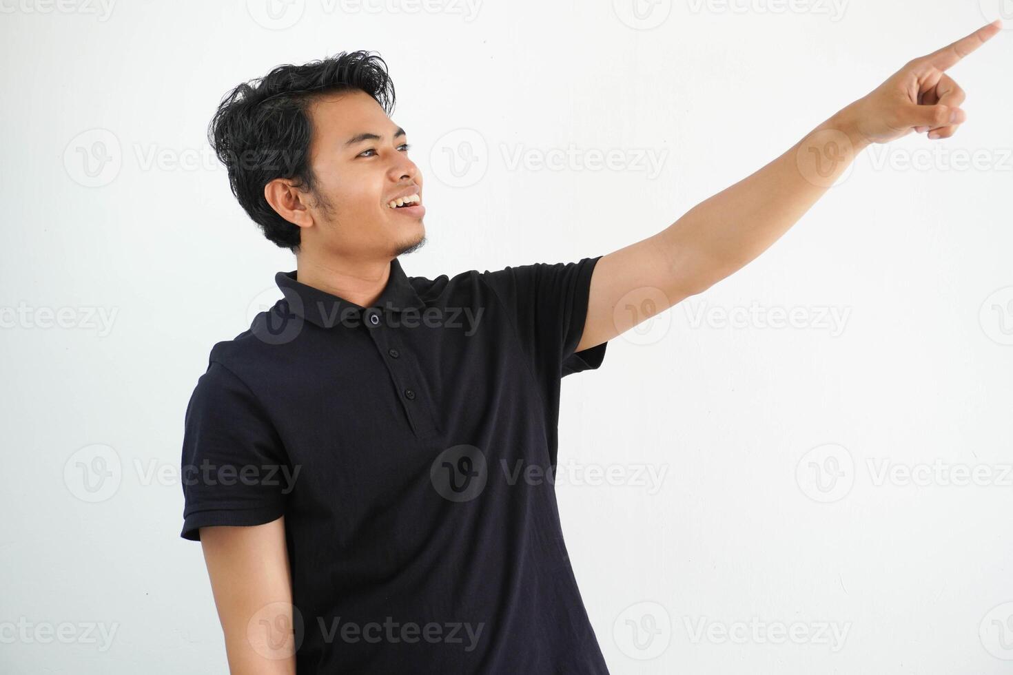 young asian man smiling confident with hand pointing to the left side wearing black polo t shirt isolated white background photo