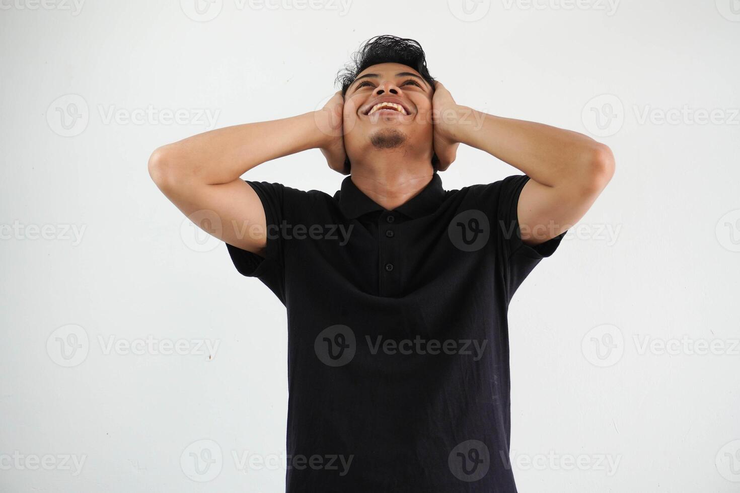 happy young asian man both hands holding the ears and look up wearing black polo t shirt isolated on white background photo