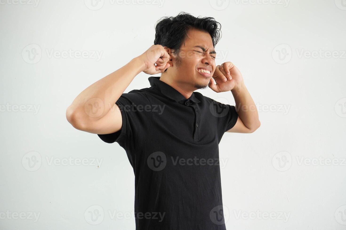 enojado joven asiático hombre cerca su orejas con dedos vistiendo negro polo t camisa aislado en blanco antecedentes foto