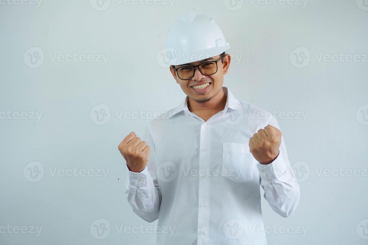 smiling or happy young asian man with clenched fist in white shirt and helmet,concept of male civil construction worker, builder, architect, mechanic, electrician posing for successful career. photo