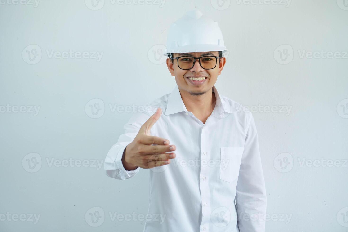 architect young asian man wearing white helmet standing over isolated white background smiling friendly offering handshake as greeting and welcoming. Successful business. photo