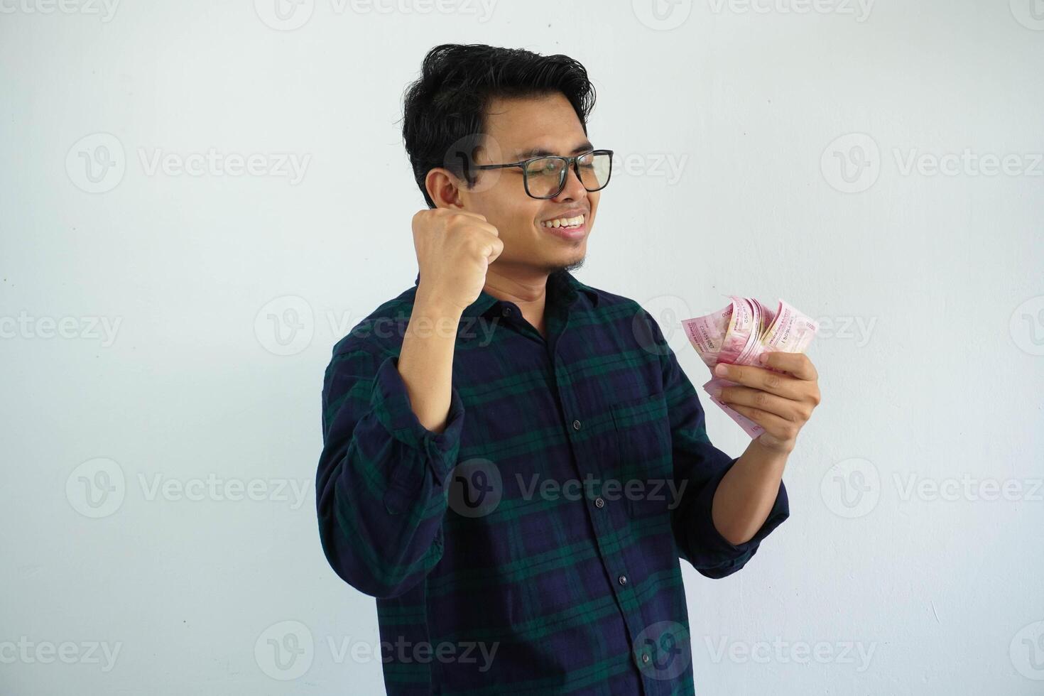 young asian man clenched fist while holding Indonesia paper money and showing excited expression isolated on white background photo