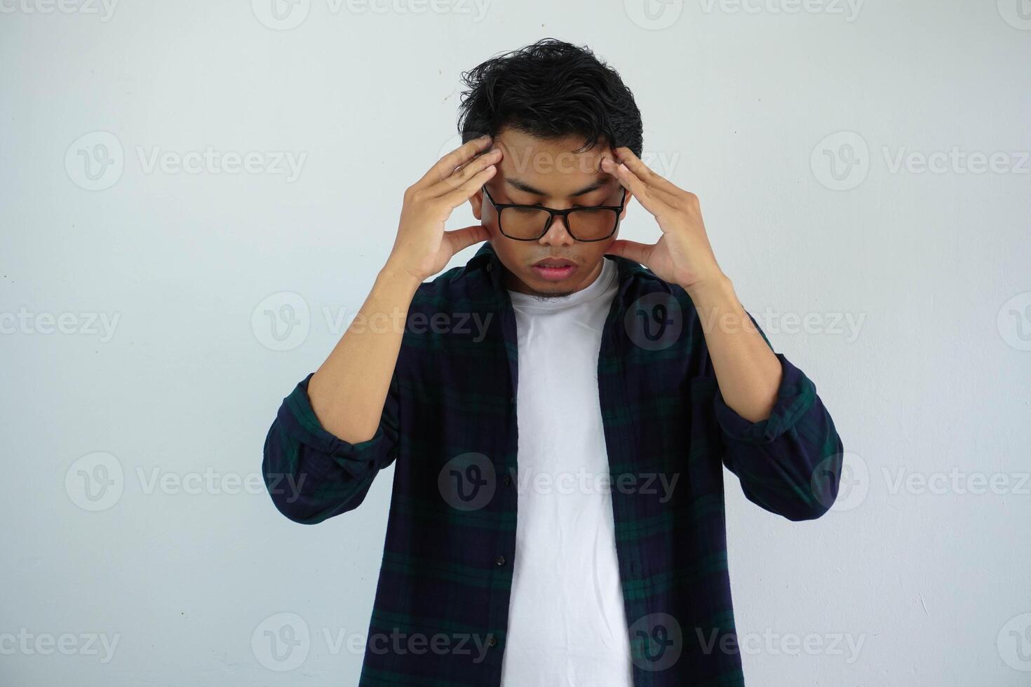 Asian youth with glasses showing pained expression while touching his head isolated on white background. photo