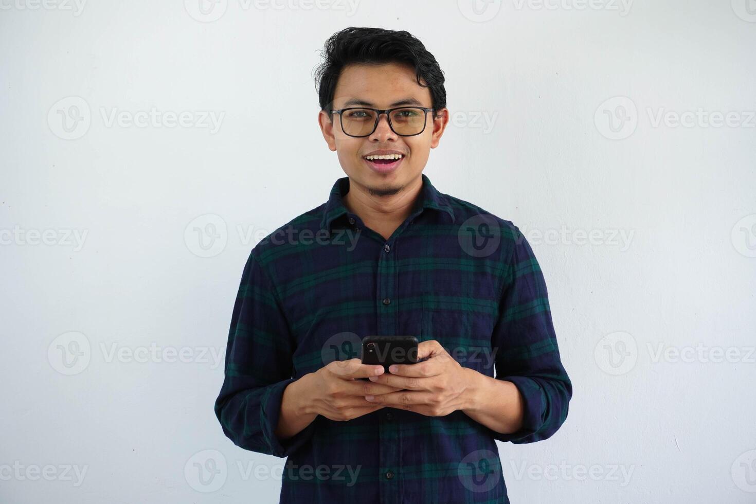 sonriente o contento joven asiático hombre participación móvil teléfono con mirando cámara aislado en blanco antecedentes foto