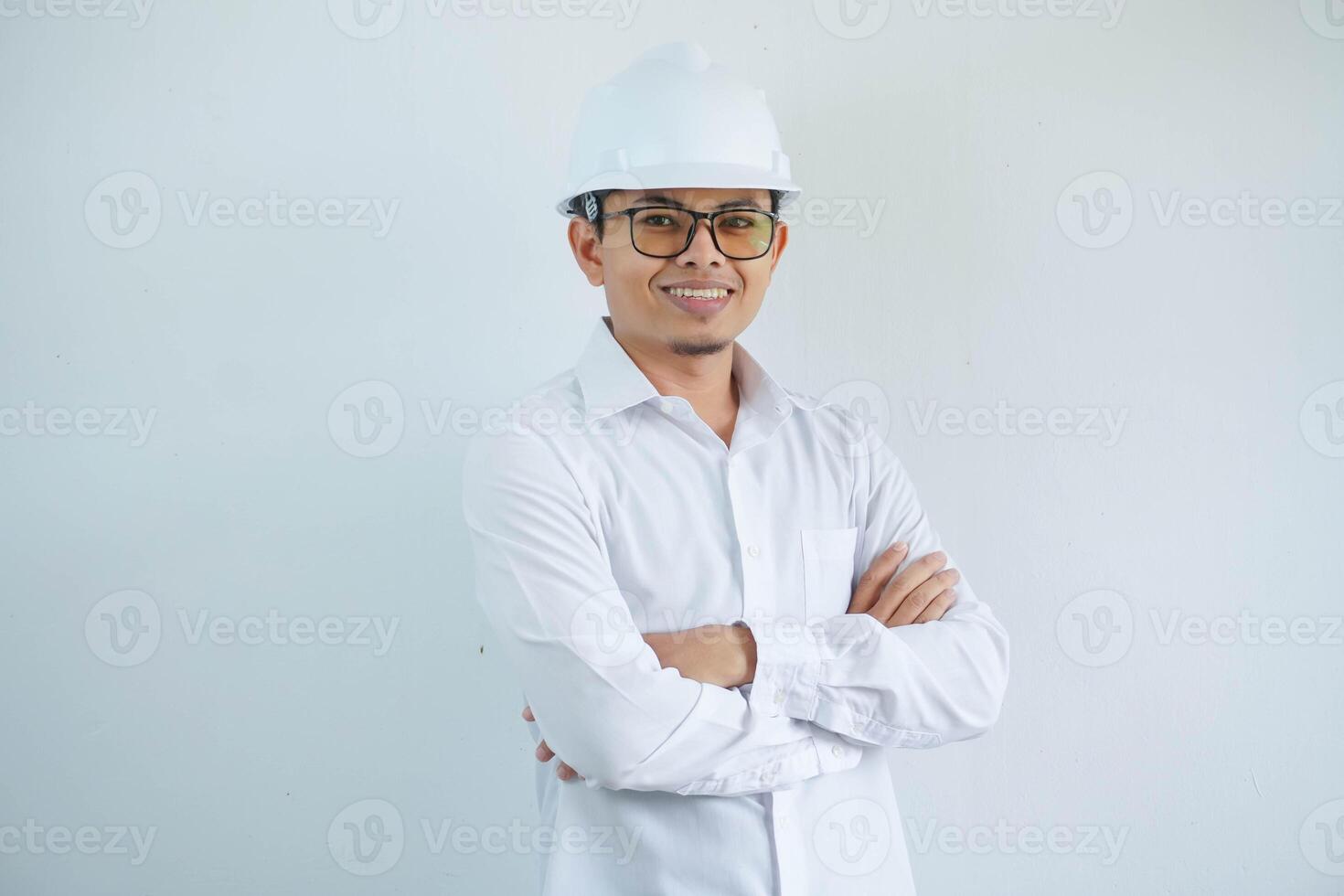 joven asiático hombre es ingeniero vistiendo casco en pie con cruzado brazos y sonriente con seguro, arquitecto o contratista, trabajador o mano de obra, industrial concepto. foto