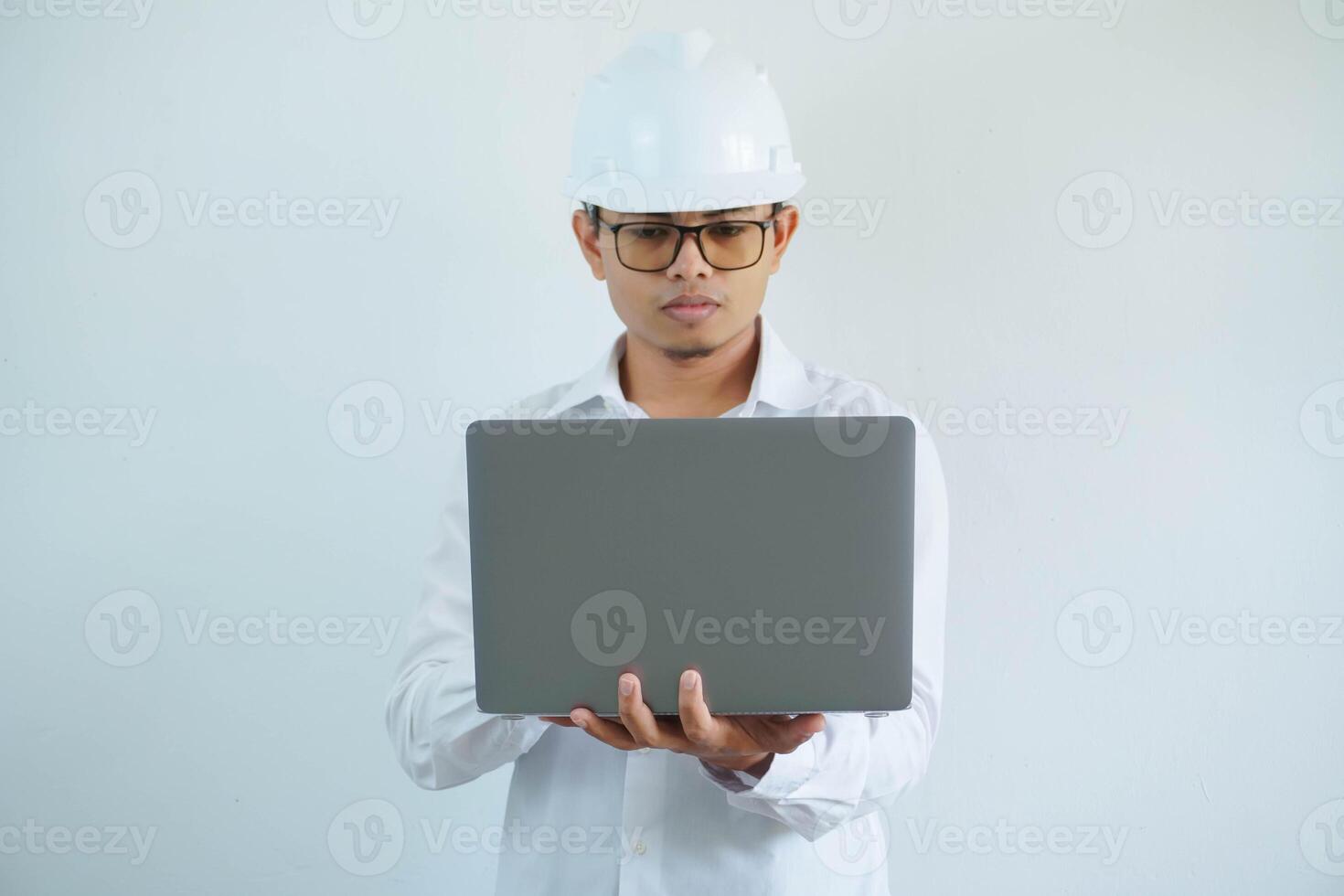 serious young asian architect man wearing builder safety helmet typing on the laptop isolated on white background photo