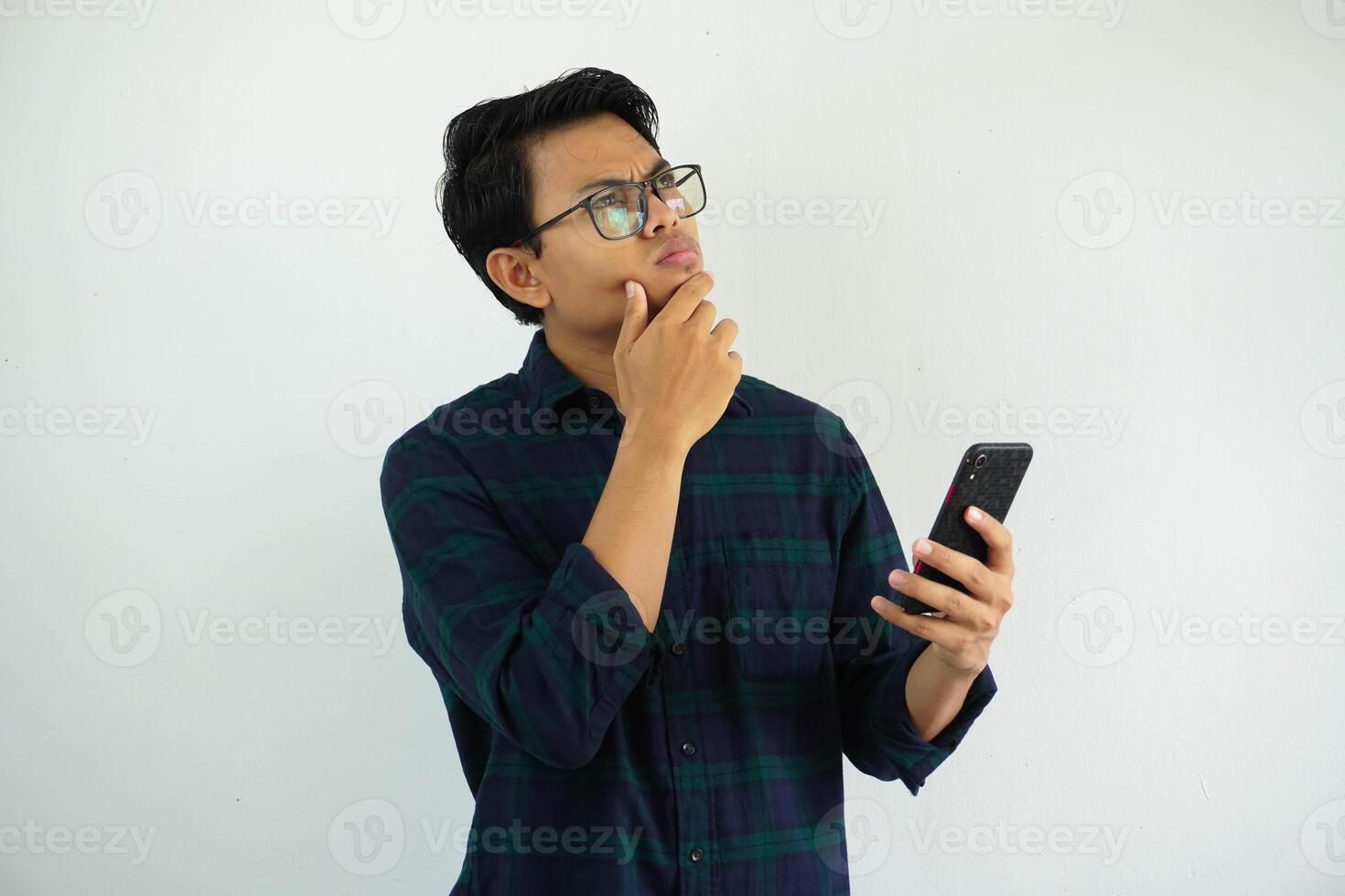 serious expression young asian man thinking something with while holding mobile phone isolated on white background. photo