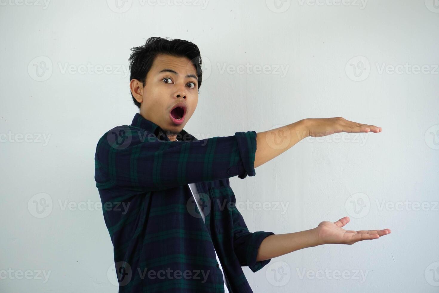 young asian man posing on a white backdrop shocked and amazed holding a copy space between hands. photo