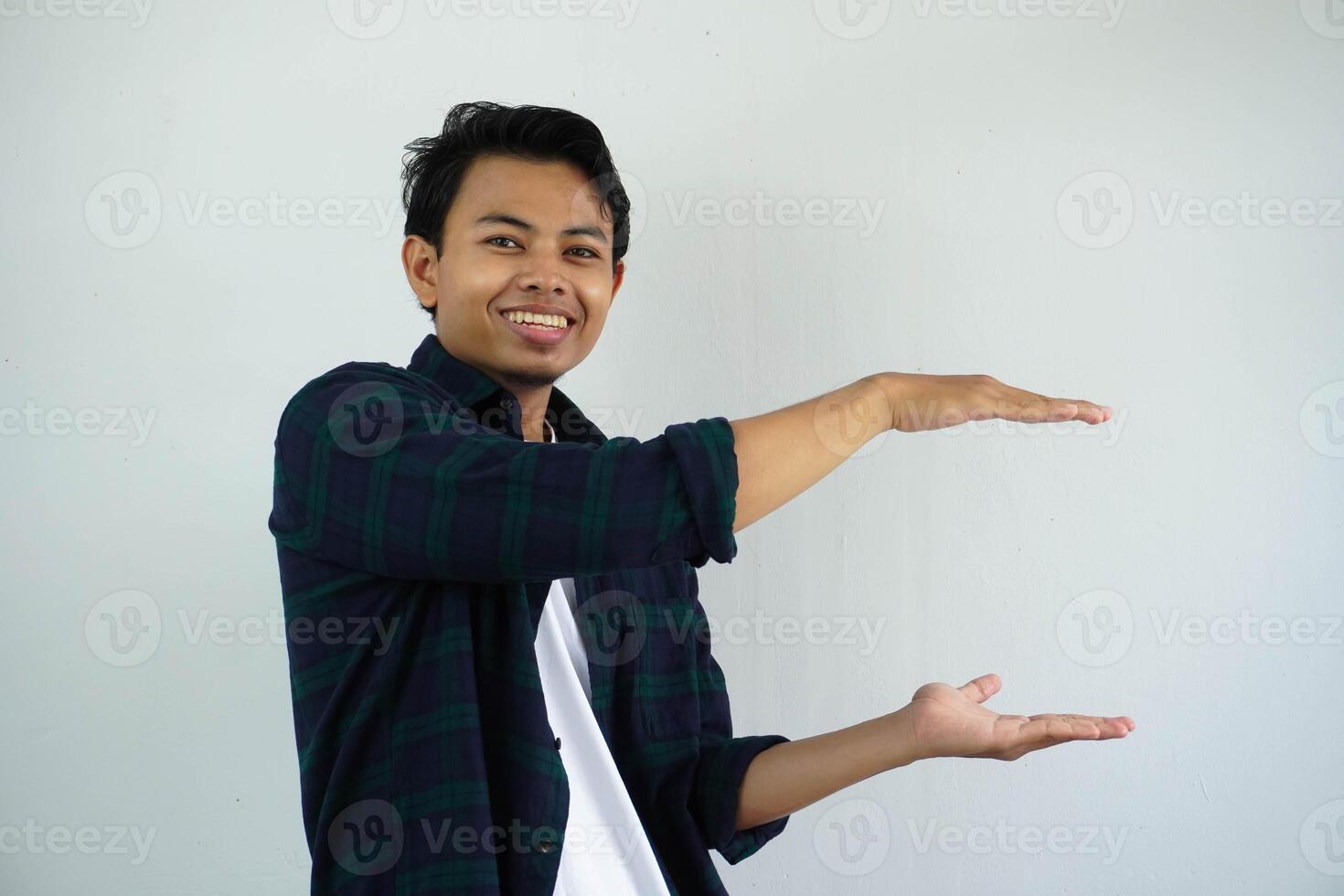 young asian man posing on a white backdrop smiling and happiness holding a copy space between hands. photo