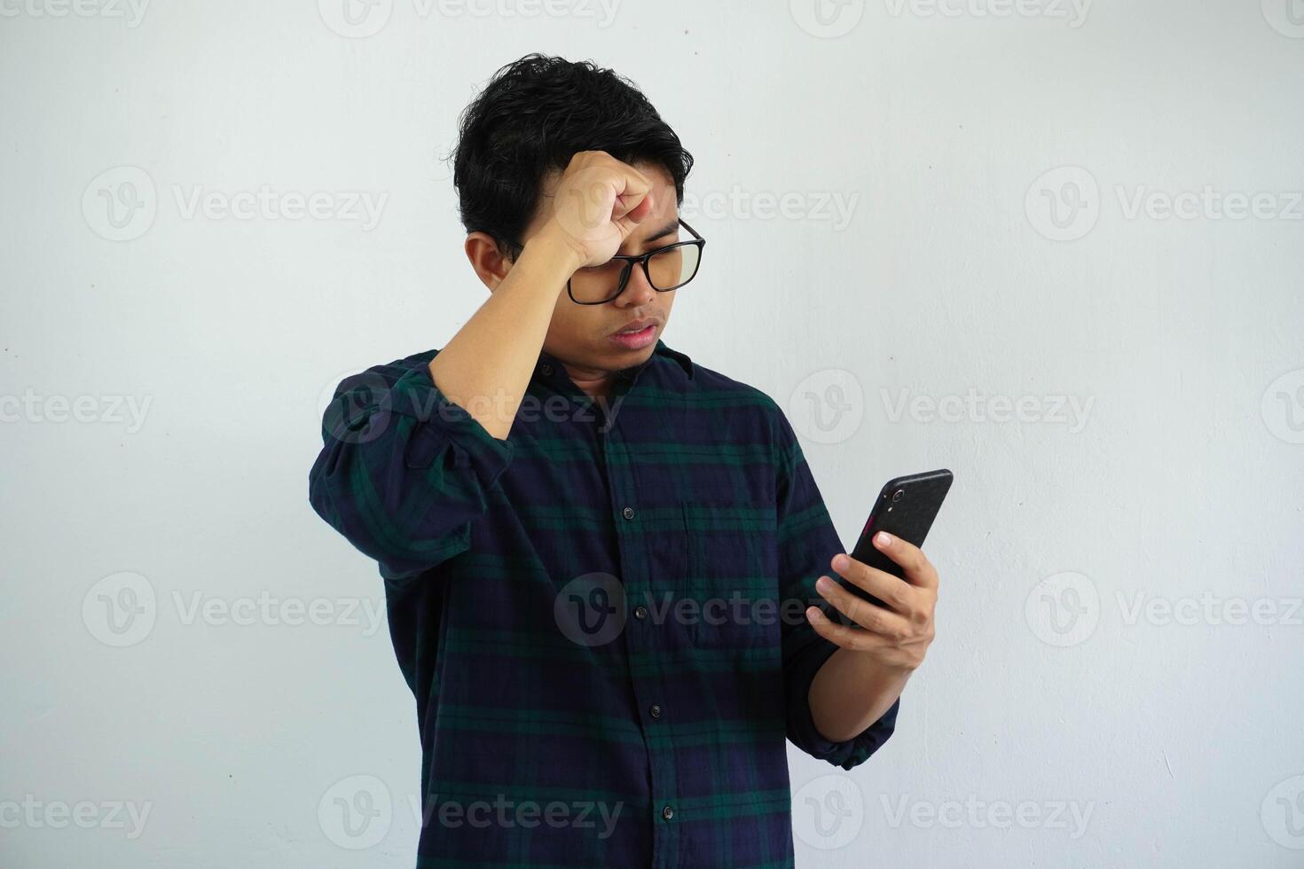 stress expression young asian man while hand touching forehead with holding mobile phone isolated on white background. photo