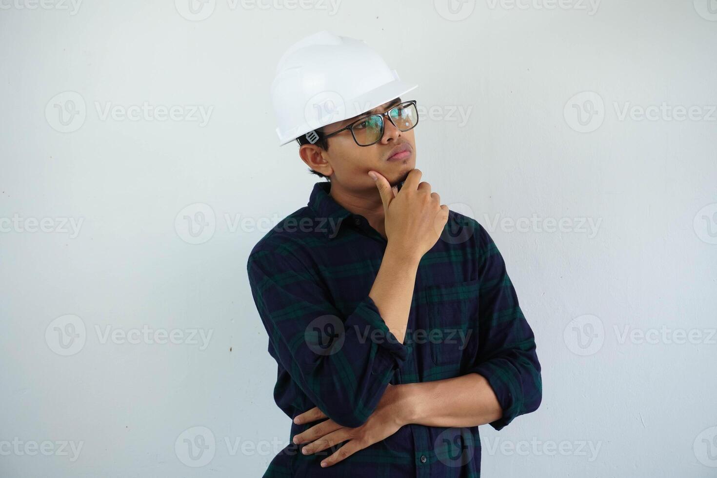 young Asian male engineer wearing white hard hat holding chin thinking for construction work isolated on white background, copy space. photo