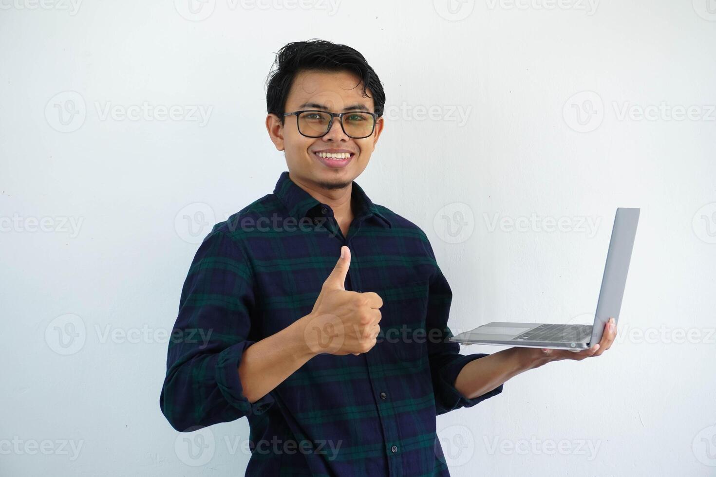 young asian man smiling confident and give thumb up while holding a laptop computer isolated on white background. photo